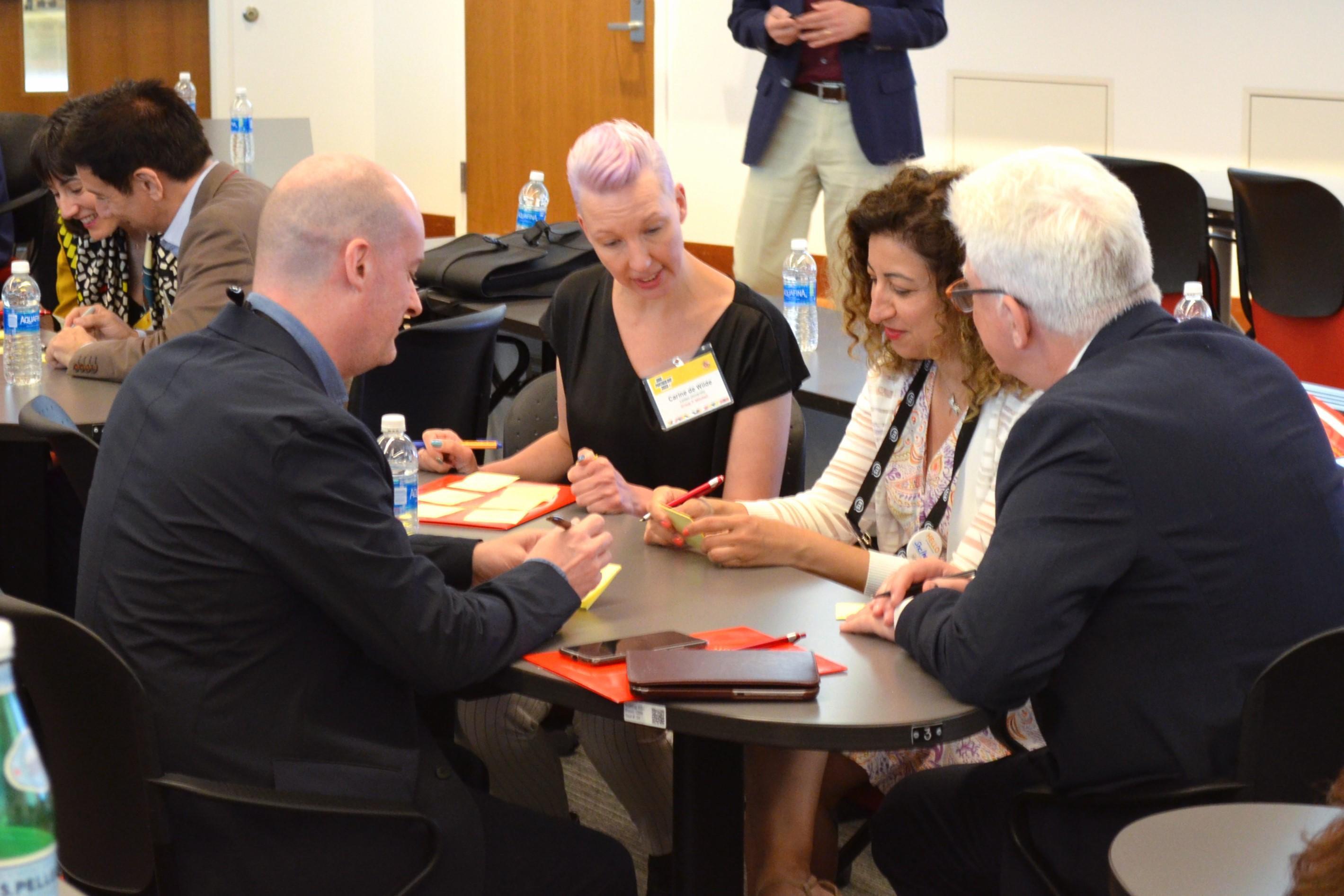 Higher education professionals from partner institutions gather around a table in discussion