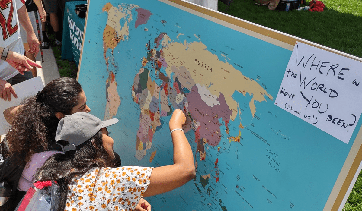 Two women place pins in a large world map.
