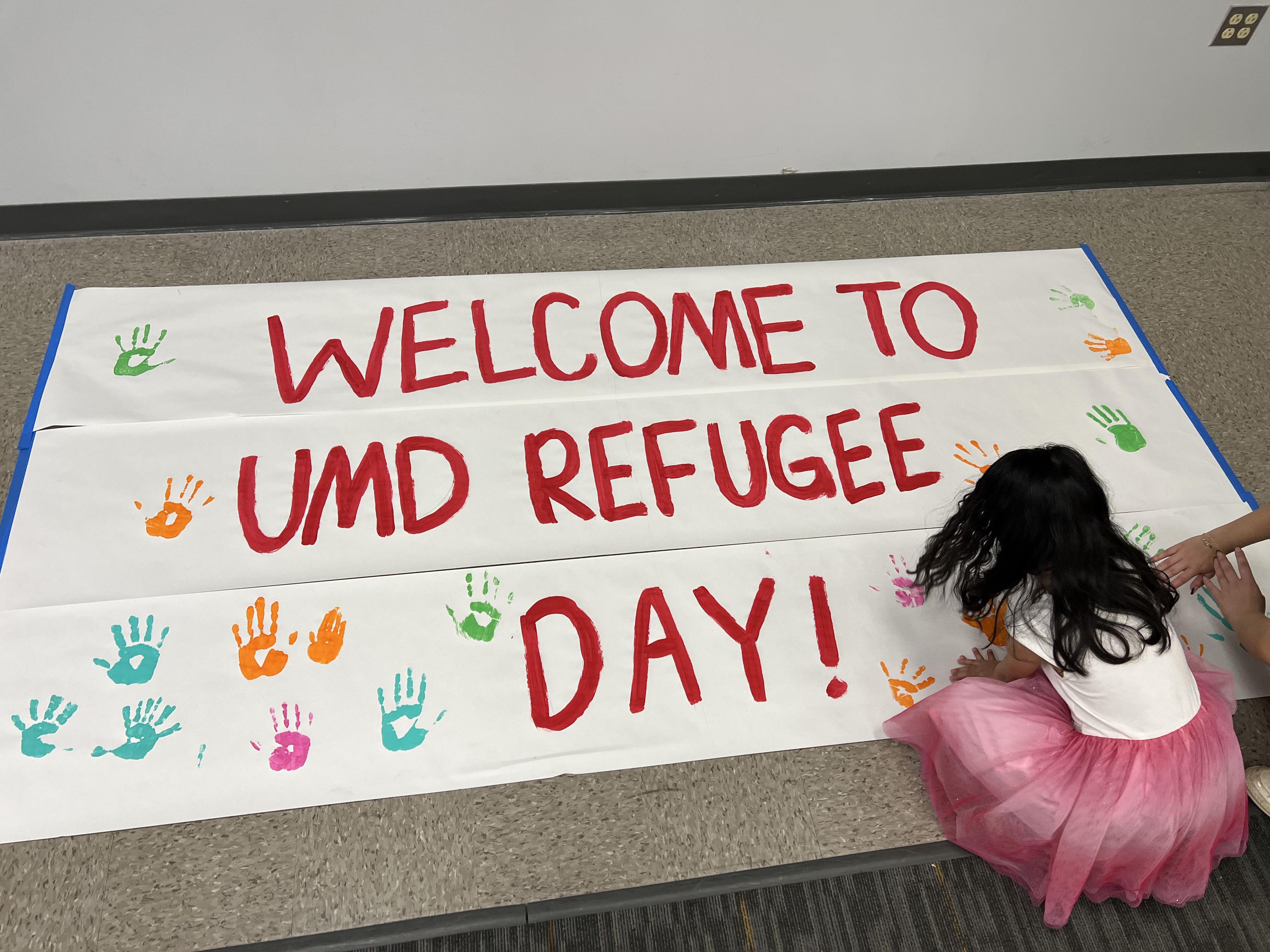 A child puts their handprints onto a tapestry reading "Welcome to UMD Refugee Day".